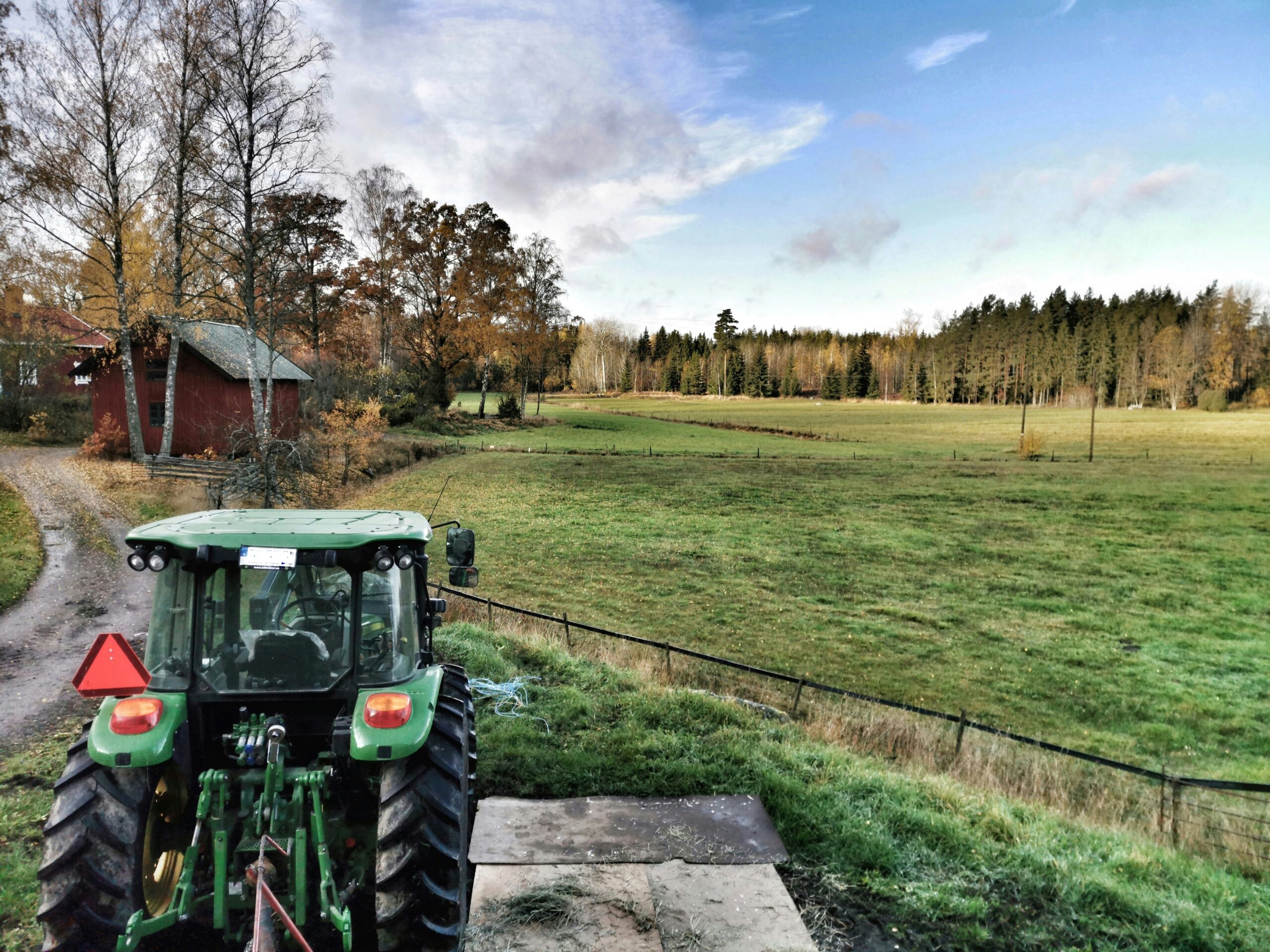 Traktor framför grusväg och lantbruk.
